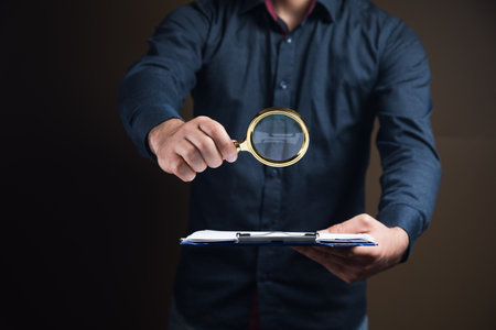 a man with a magnifying glass looks at papers on a brown backgroundの写真素材