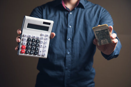 a man makes calculations on a cooler and holds money on a brown backgroundの写真素材