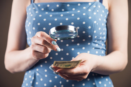 woman examines the money with a magnifying glass. counterfeit check conceptの写真素材