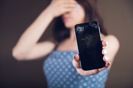 young woman showing broken phone covering her faceの写真素材