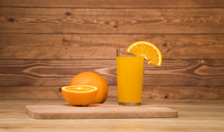 on a wooden table an orange and a glass with a drinkの写真素材