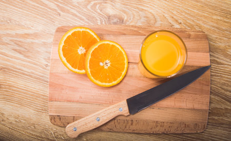 on a wooden table a knife, a glass with a drink and an orangeの写真素材