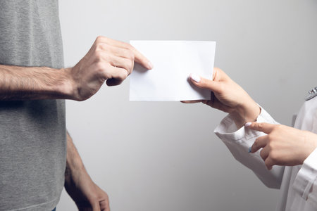 a man gives an envelope to a doctor on a gray backgroundの写真素材