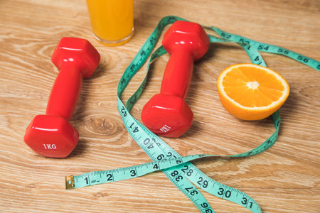 measuring tape, dumbbell, orange and orange juice on the tableの写真素材