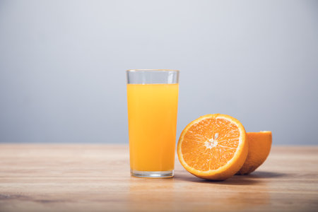 on a wooden table an orange and a glass with a drinkの写真素材