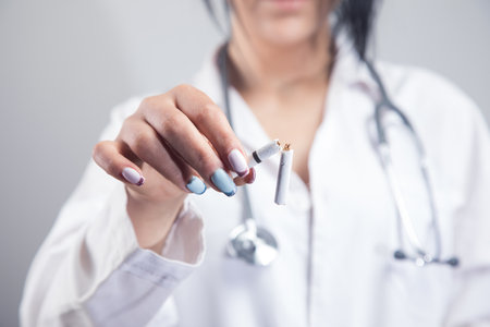 female doctor holding broken cigarette on gray backgroundの写真素材