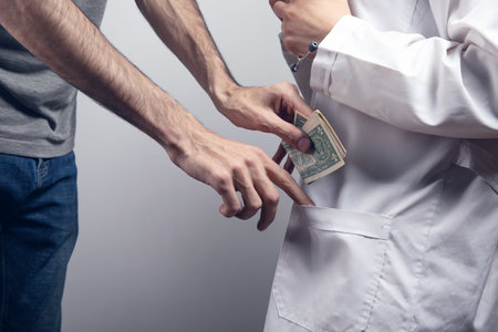 the man puts money in the pocket of the doctor. bribe concept on gray backgroundの写真素材