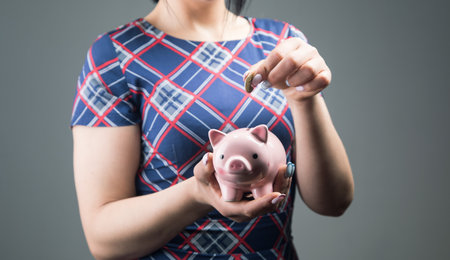 a woman in a dress throws a coin into a piggy bank on a gray backgroundの写真素材