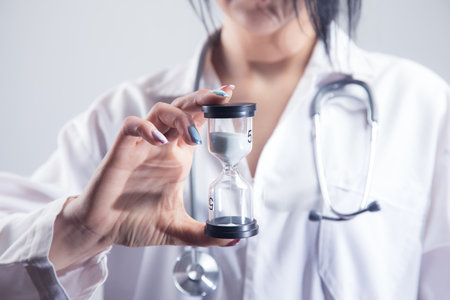 female doctor holding hourglass on gray backgroundの写真素材