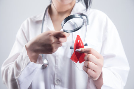 the doctor looks at the red tape with a magnifying glass. aids study concept on gray backgroundの写真素材