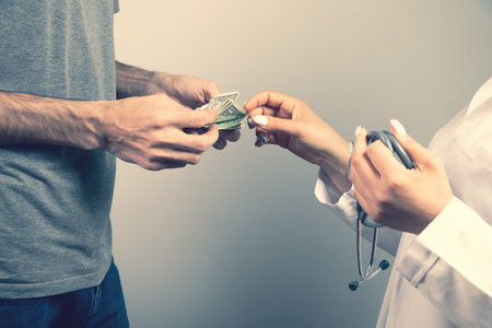 a man gives money to a doctor on a gray backgroundの写真素材