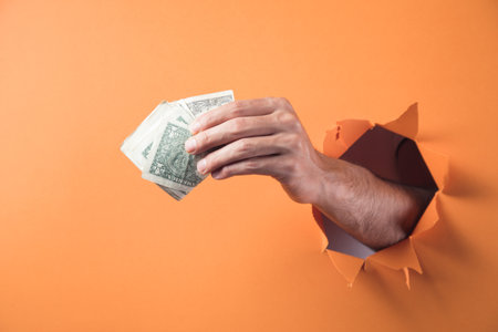Hand holds money on orange backgroundの写真素材
