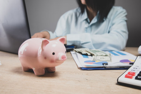 a woman sits in front of a piggy bank at a deskの写真素材