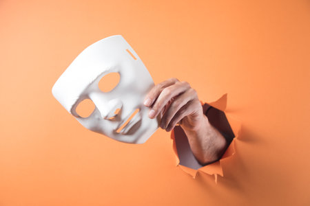 hand holds white mask on orange backgroundの写真素材