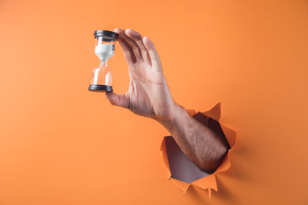 hand holds hourglass on orange backgroundの写真素材