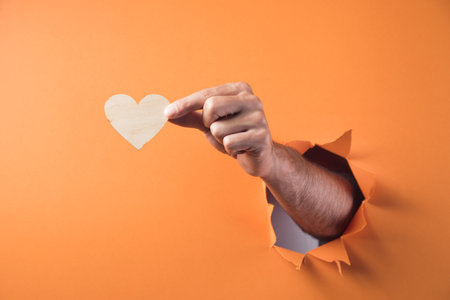 Hand holds a wooden heart on an orange backgroundの写真素材