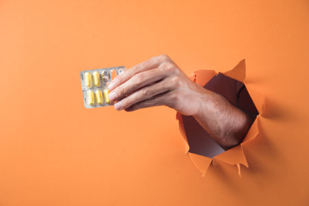Hand holds pills on orange backgroundの写真素材