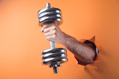 hand holds dumbbell on orange backgroundの写真素材