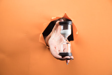 female hand holds hourglass on orange backgroundの写真素材