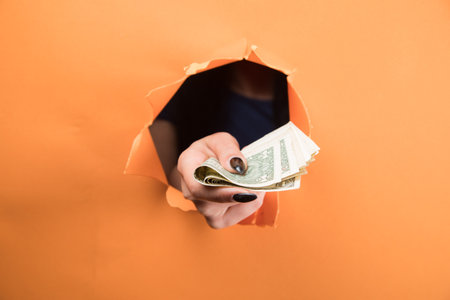 female hand holding a dollar bill on an orange background