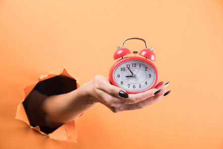 female hand holding alarm clock on orange background