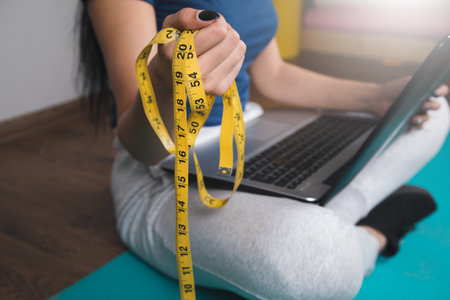 woman holding measuring tape on mat in front of laptop