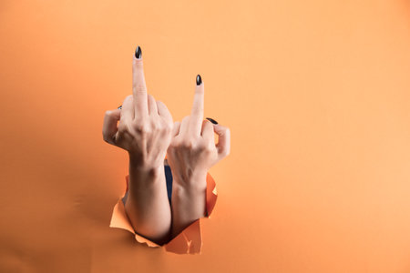 female hand shows middle finger on orange backgroundの写真素材