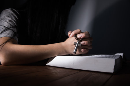 woman praying on a book and holding a crossの写真素材