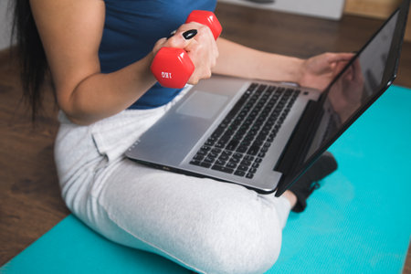 woman holding dumbbell on mat in front of laptopの写真素材
