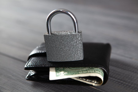 lock on a black wallet on a wooden table. money safety conceptの写真素材