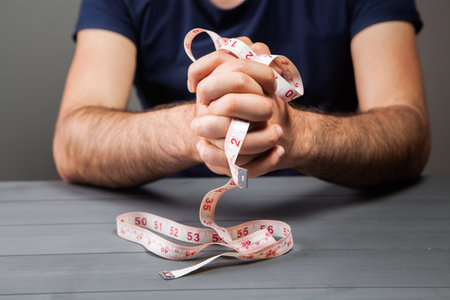 man holding a measuring tape in his hands on a gray backgroundの写真素材