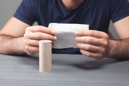 man holding the last piece of toilet paper on gray backgroundの写真素材