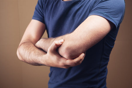 a young guy has a sore elbow on a brown backgroundの写真素材