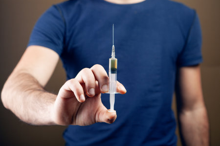 man holding a filled syringe. addiction concept on brown backgroundの写真素材