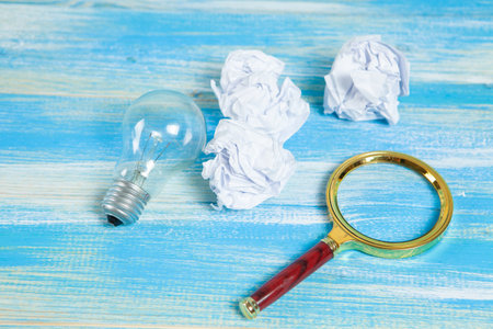 light bulb, crumpled papers and a magnifying glass. concept search for ideas in trash on wooden backgroundの写真素材