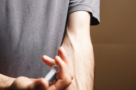 drug addict gives himself an injection on brown backgroundの写真素材