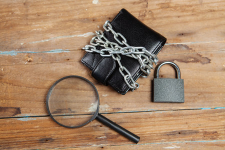 magnifying glass looks at a wallet in chains, closed with a padlock on the tableの写真素材