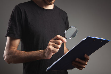 a man with a magnifying glass looks at papersの写真素材