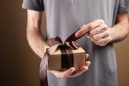 man opens gift ribbon on brown backgroundの写真素材