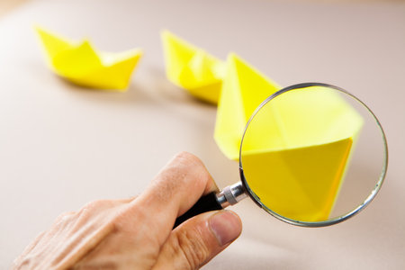 yellow paper boats and a magnifying glass on the tableの写真素材