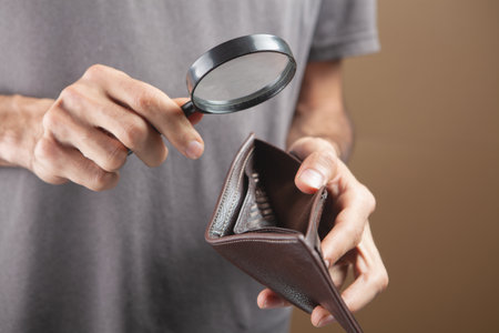 man looking at empty wallet with magnifying glass on brown backgroundの写真素材
