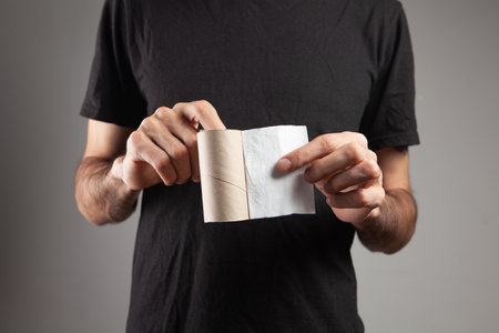 man holding the last piece of toilet paper on gray background