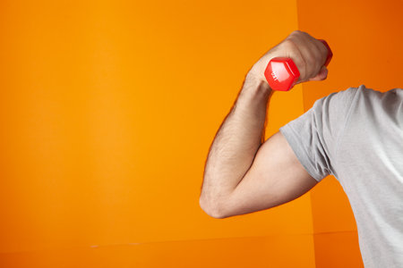 man holding small dumbbells on orange backgroundの写真素材