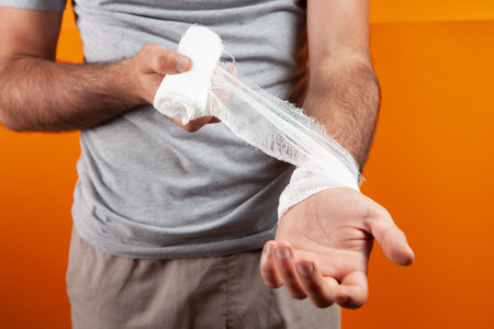 man tied his hand with a bandage on a orange backgroundの写真素材