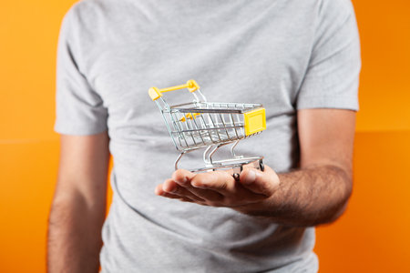a man holds a cart in his hand. shopping concept on orange backgroundの写真素材