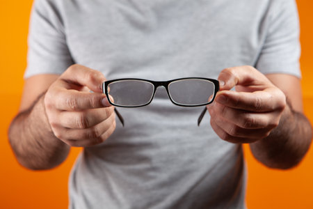 young guy holding optical glasses on orange backgroundの写真素材