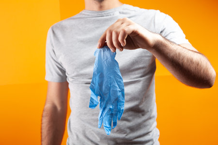 man putting on rubber gloves on orange background