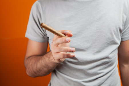 man holding  cigar in his hands on an orange backgroundの写真素材