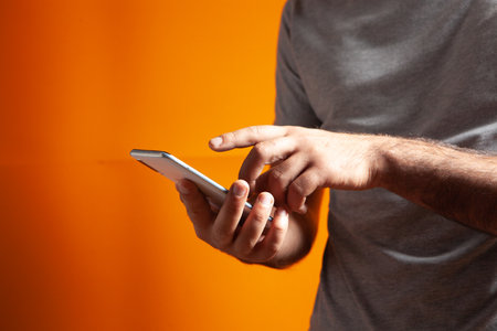man presses on the phone screen on an orange backgroundの写真素材