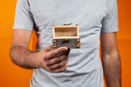 man holding small treasure chest on orange backgroundの写真素材